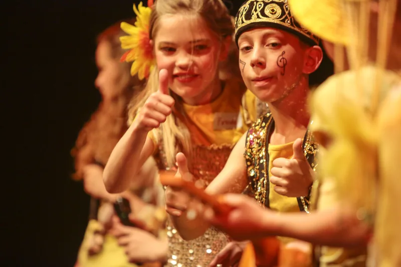Twee geschminkte kinderen in geel kostuum kijken lachend opzij