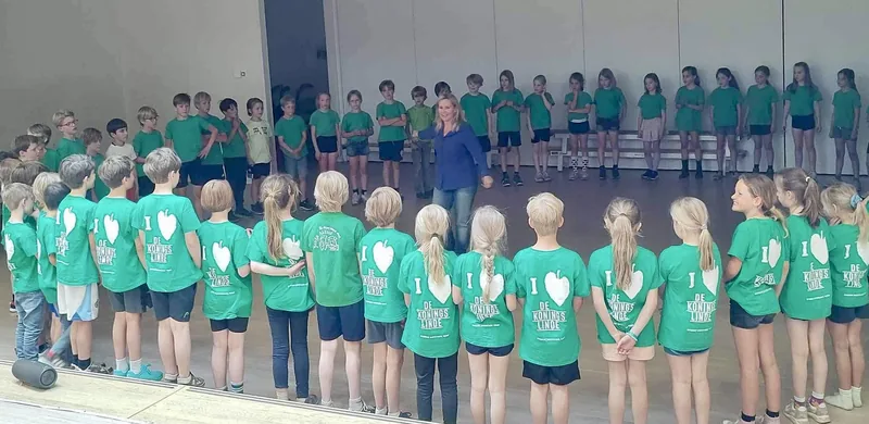 Grote groep kinderen in groene shirts staat in een lange rij in de gymzaal