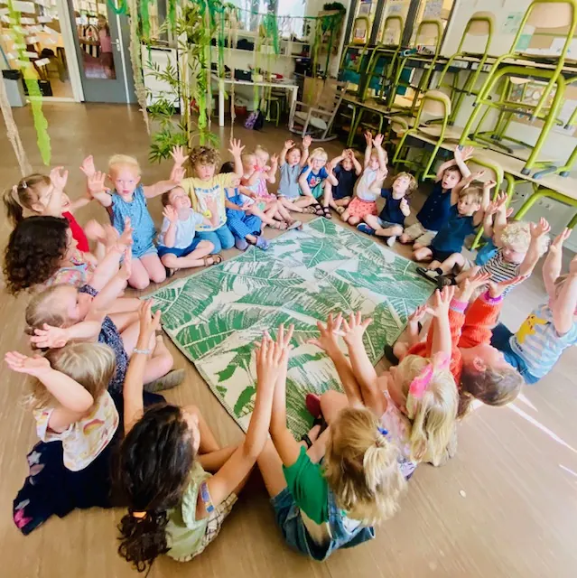 Grote groep kinderen in een kring met de handen omhoog